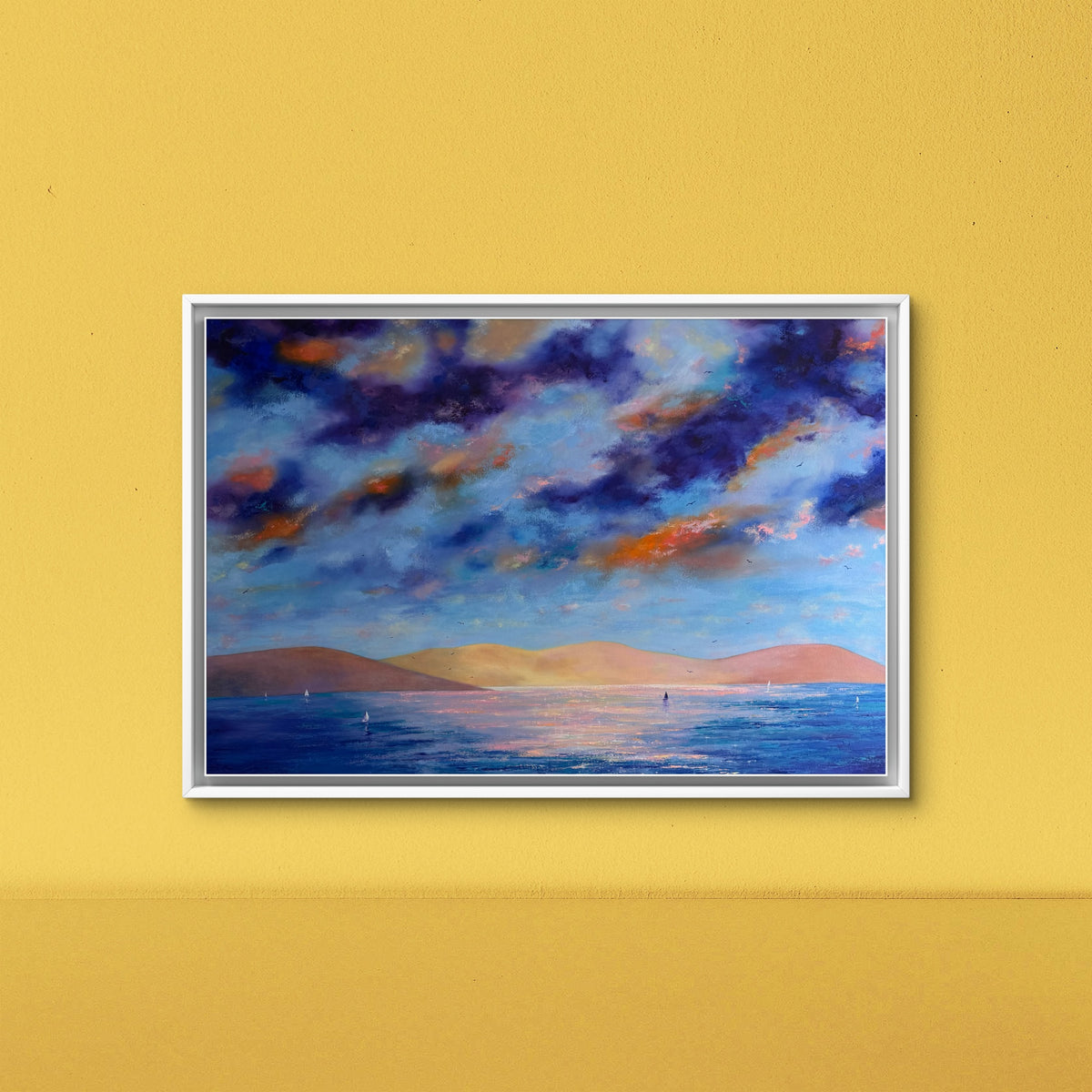 A framed landscape painting of a seascape under a dramatic blue and purple sky with orange clouds, displayed on a textured yellow wall.