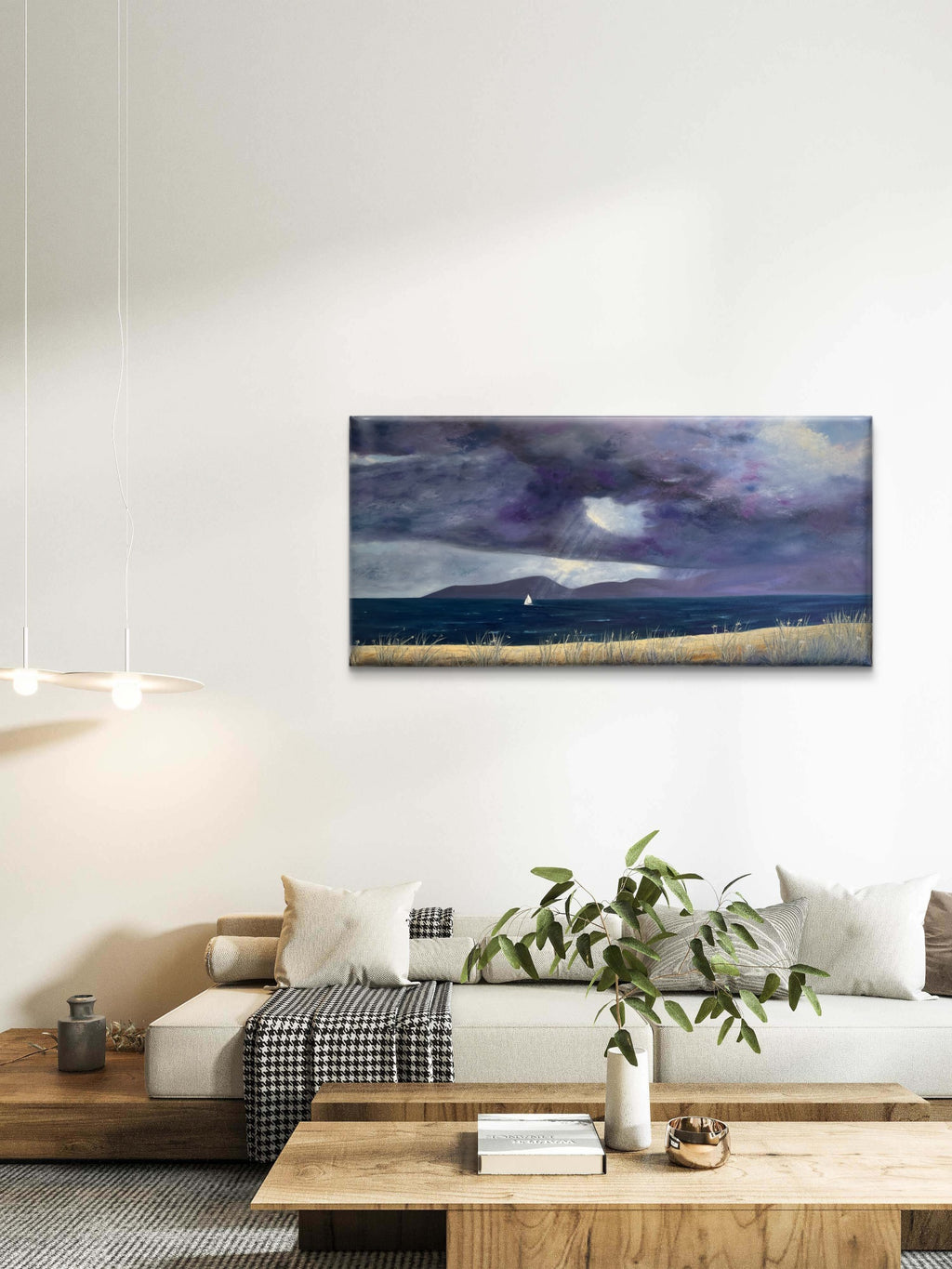 A horizontal landscape original oil painting featuring a stormy purple and blue sky over a field, displayed on a white wall above a modern white sofa in a styled living room.
