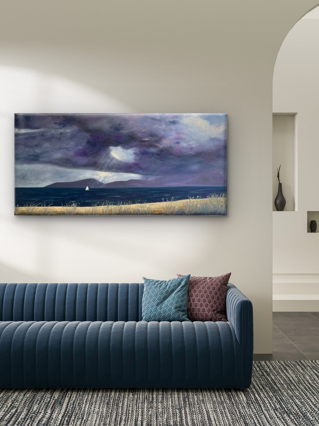 A panoramic original oil painting on canvas of a dramatic purple and blue stormy seascape with a sailboat, displayed on a beige wall above a modern blue ribbed sofa in a styled living room.