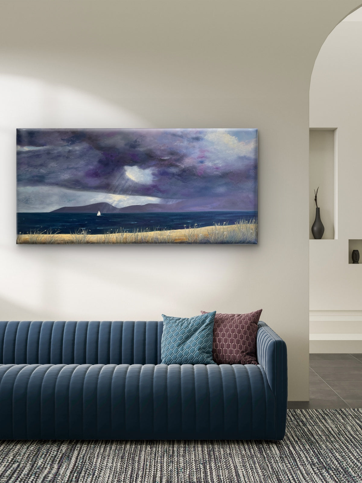 A panoramic original oil painting on canvas of a dramatic purple and blue stormy seascape with a sailboat, displayed on a beige wall above a modern blue ribbed sofa in a styled living room.