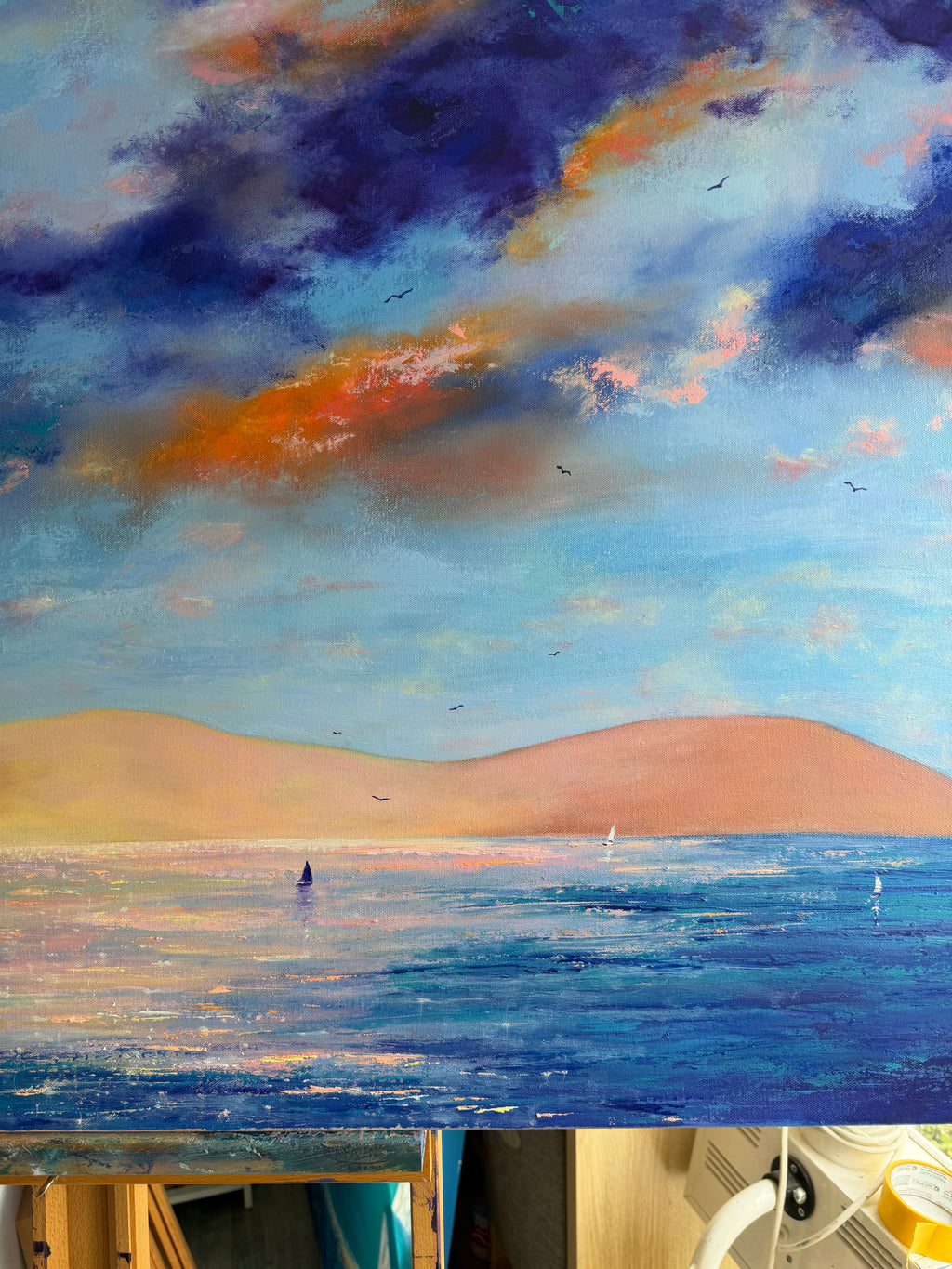 An impressionistic landscape painting of a seascape under a dramatic cloudy sky, with blue water, soft pink hills, and deep blue and orange clouds.